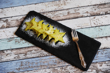 Carambola pieces served with icing sugar on a black slate plate
