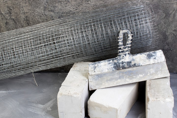 roll mesh for plastering, putty knife bricks, hammer on the gray concrete background. Copy space....