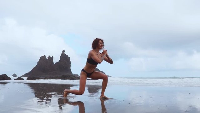 Along the ocean female exercisers performing lunges alternating each leg on the background of rocks and water. Training for weight loss during the resort on the island