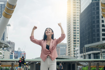 Fototapeta na wymiar Business woman happy celebrating successful business with arms spread out winning and overlooking the city center high-rises.