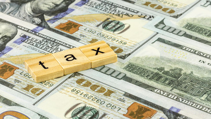 Tax Concept with wooden block on dollar bills.