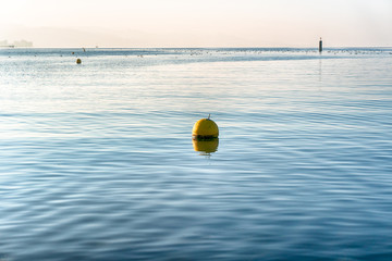 minimalist view of blue lake with blue sky and yellow floating buoy and distance marker