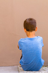 Sad alone boy sitting on the ground behind the wall outdoor