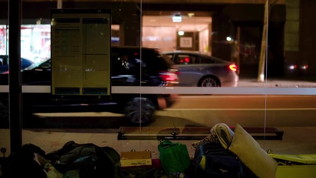 Tilt to Reveal Homeless Person's Belongings Under a Bus Stop