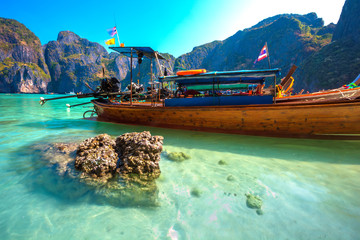 Brown stone in crystal clear transparent turquoise water next to long-tailed boats in a beautiful famous bay on the backdrop of Thai tropical mountains. Maya Bay, Phi Phi Leh island, Krabi, Thailand.