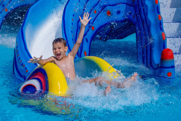 Little happy boy with hands up sliding into water in aqua park