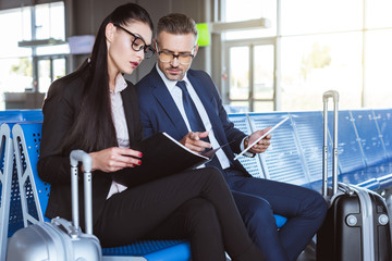 adult businessman using digital tablet while businesswoman holding black folder at departure lounge in airport