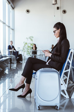 young businesswoman in glasses with smartphone sitting at departure lounge in airport
