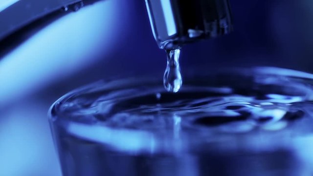 Water dripping in slow-motion from a kitchen tap. Blue tinted. Close up.