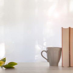 Thick books, a gray cup with coffee and twigs with green leaves on a wooden table lit by the sun. Copy space