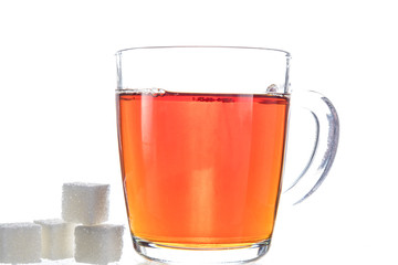 Transparent mug with tea on a white background next to the pieces of sugar