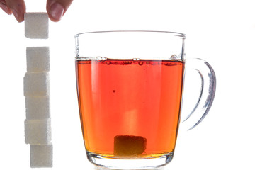 Transparent mug with tea on a white background next to the pieces of sugar