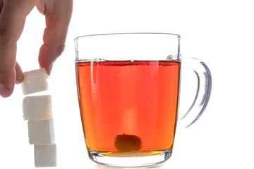 Transparent mug with tea on a white background next to the pieces of sugar