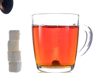 Transparent mug with tea on a white background next to the pieces of sugar