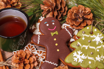 Christmas background. Tea in a metal green mug, traditional Christmas gingerbread, Christmas tree branches and cones on a wooden background close-up, top view