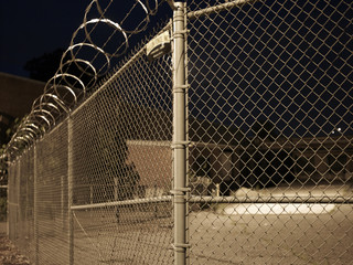 Close up of a chain link barbed wire fence in front of a yard at night
