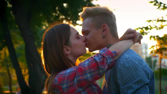 Lovely couple is kissing calmly while standing in beautiful pakk outdoor, sunlights, casual look