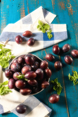 Ripe juicy plums on a plate, on old blue wooden table.