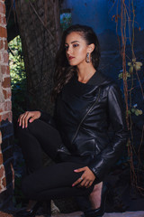 Obraz premium A beautiful girl with long hair in a long black dress with white wings in the image of an angel sits on the stair railing near the walls of an old mansion.