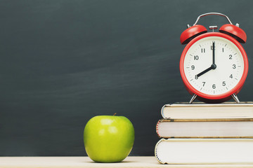 apple green,alarm clock red on book, put on the desk wooden stationery blackboard background. Education back to school concept. Leave empty copy space for text.