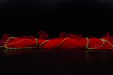Red fabric and golden Christmas decoration chord on black.