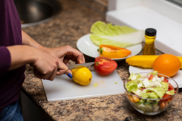 Female hand cuts vegetables for salad.