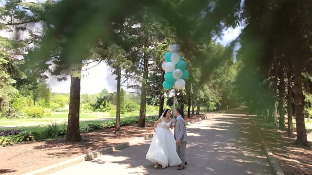Portrait of happy newlyweds in the summer Park, they walk and enjoy the good weather. Happy newlyweds walking in the Park with balloons. Portrait of happy newlyweds in a Sunny summer Park.