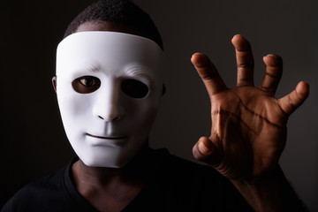 Studio shot of young black African man in dark room wearing mask