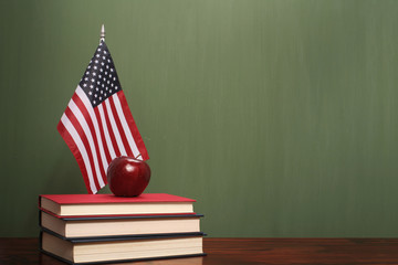 Books, US flag, and a red apple in front of a green chalkboard