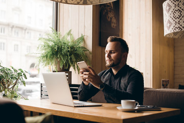 Young handsome man sitting in office with cup of coffee and working on project connected with modern cyber technologies. Businessman with notebook trying to keep deadline in digital marketing sphere.