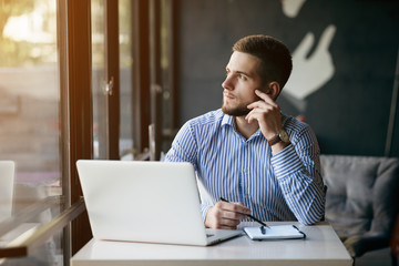 Young man drawing template for the web site associated with digital marketing, current trends and tendencies of UX / UI design. Businessman who rules his company remotely, like a freelancer