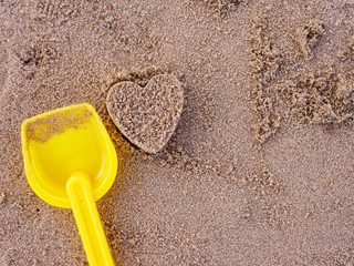 Fototapeta na wymiar heart shape on beach sand with kid toy for family holiday concept 