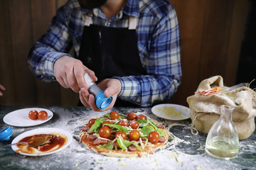 man preparing a pizza, knead the dough and puts ingredients