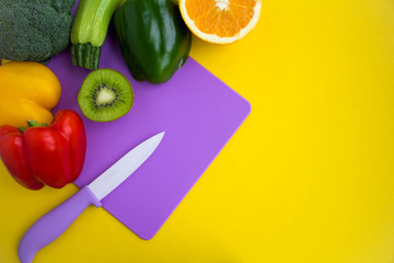 Vegetables and fruits on the violet  cutting board  on the yellow background.Top view.Copy space.