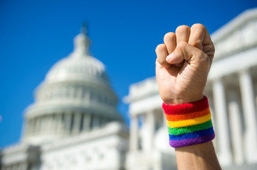 Hand wearing gay pride rainbow wristband making a power fist gesture in front of the US Capitol...