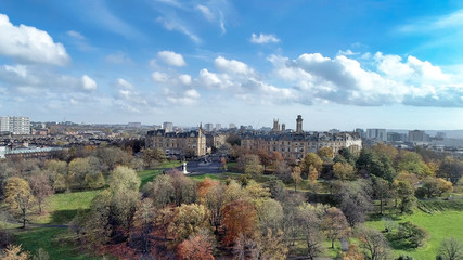 Fototapeta na wymiar Low level aerial image over the autumn foliage of trees in Kelvingrove Park, Glasgow, to the elegant buildings of Park Circus.