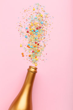 Champagne bottle with colorful sprinkles on pink background