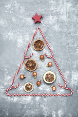 Candy canes and dry fruits in shape of christmas tree on grey wooden table