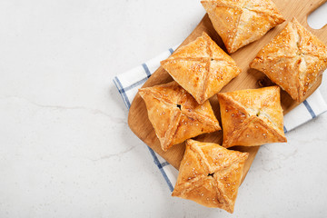 Puff pastry squares filled with potato, cheese and spinach on light gray stone table.top view