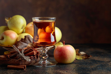 Glass of apple juice or cider with juicy apples and cinnamon sticks.