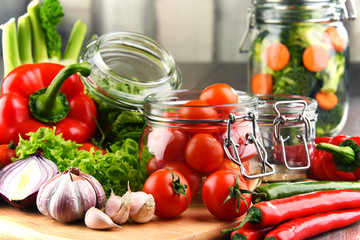 Jars with marinated food and raw vegetables on cutting board