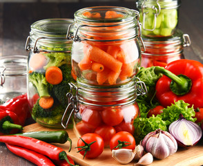 Jars with marinated food and raw vegetables on cutting board