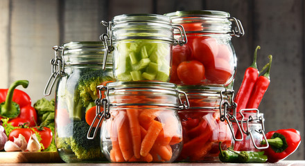 Fototapeta na wymiar Jars with marinated food and organic raw vegetables
