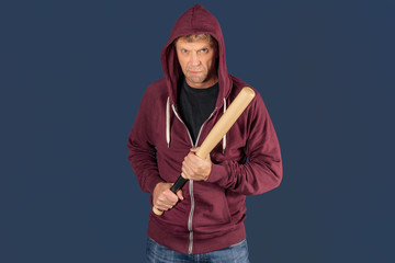 Man in sweatshirt with baseball bat ready for fight on blue background