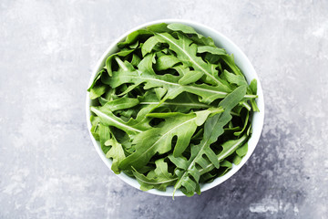 Green arugula leafs in bowl on grey wooden table