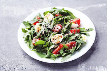Salad with arugula leafs, tomatoes and eggs on grey wooden table