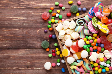 Fototapeta na wymiar Sweet candies and lollipops in basket on brown wooden table