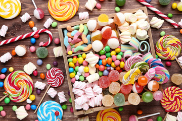 Fototapeta na wymiar Sweet candies and lollipops in basket on brown wooden table