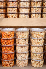 Stacked transparent plastic trays full of different kinds of nuts on the shelf of a store full of delicacies.