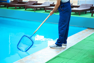 Male worker cleaning outdoor pool with scoop net